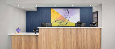 A hotel reception desk with a modern design, featuring a wooden panel backdrop and a large abstract artwork above it.