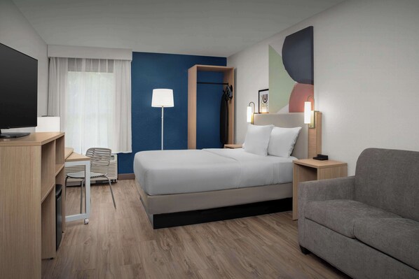 A modern hotel room with a bed, a desk, a chair, a sofa, and a TV.