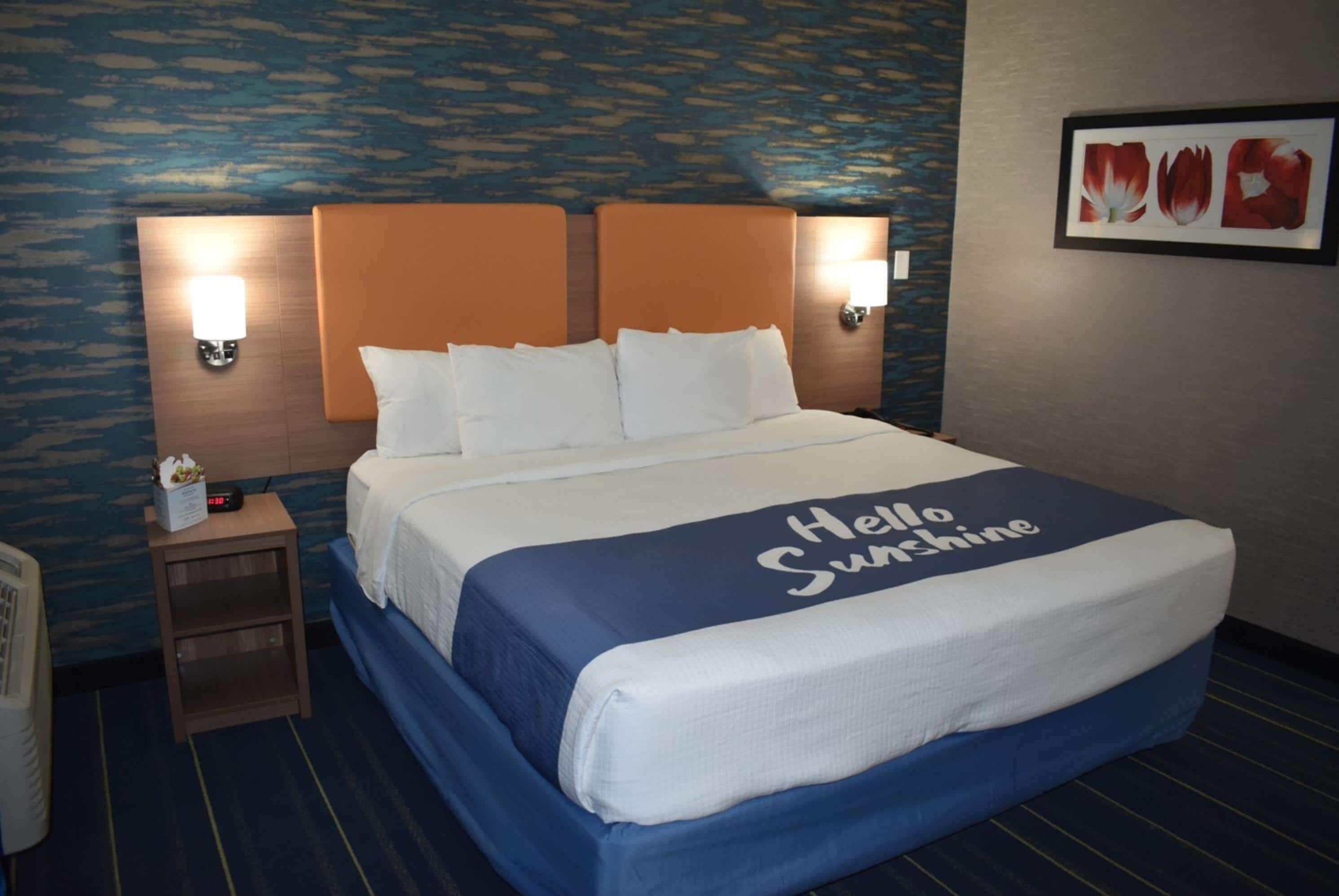 A hotel room with a bed, two wall-mounted lamps, a nightstand, and a framed picture on the wall.