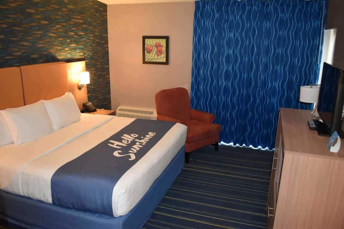 A hotel room with a bed, a chair, a desk with a computer, and a curtain.