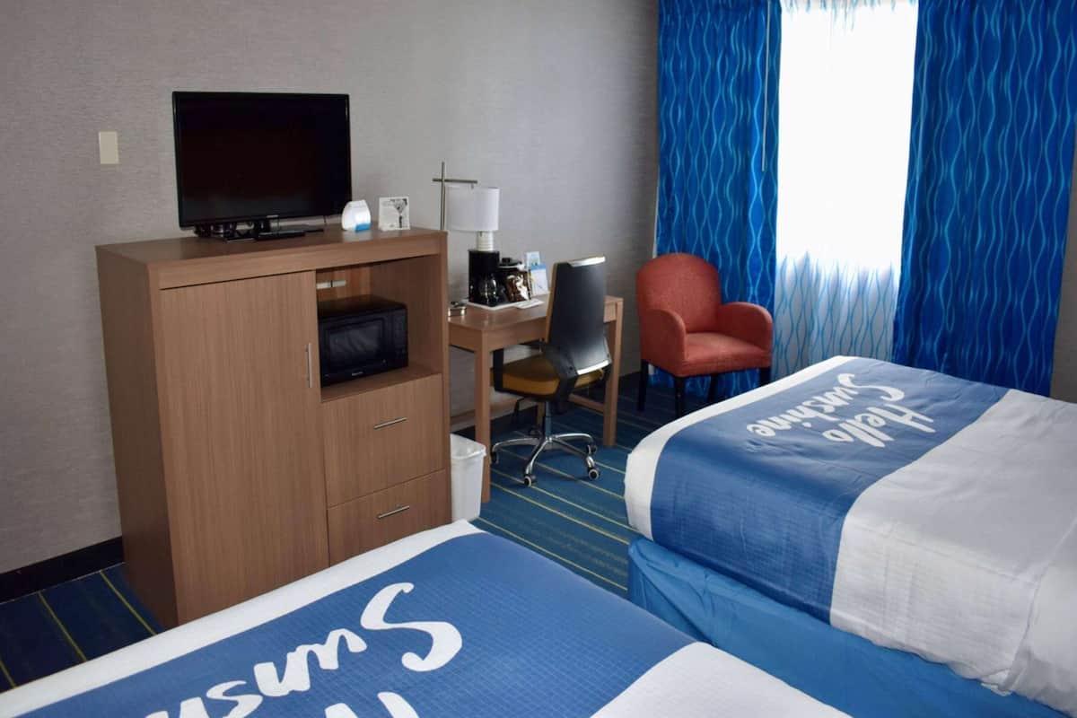 A hotel room with a bed, a desk with a television, a chair, and a window with blue curtains.