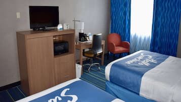 A hotel room with a bed, a desk with a television, a chair, and a window with blue curtains.