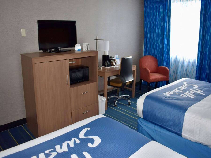 A hotel room with a bed, a desk with a television, a chair, and a window with blue curtains.