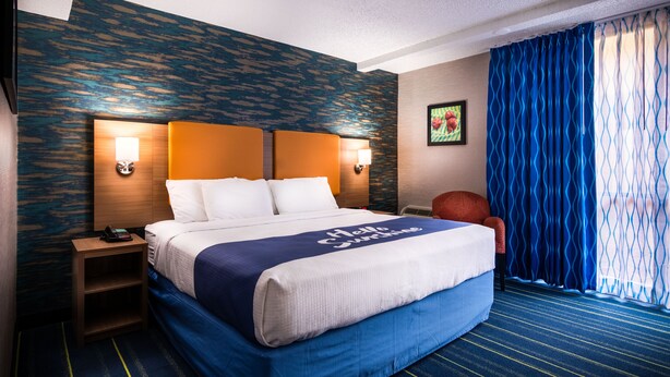 Habitación de hotel con una cama grande, dos lámparas de noche, una mesita, una silla y una ventana con cortinas azules.