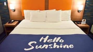 A hotel room with a bed featuring a 'Hello Sunshine' bedspread, two nightstands, a phone, and a clock.