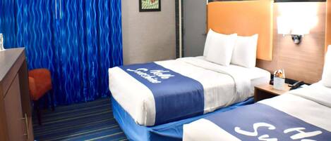 A hotel room with two beds, a blue-striped carpet, a wooden headboard, and a wall-mounted lamp.