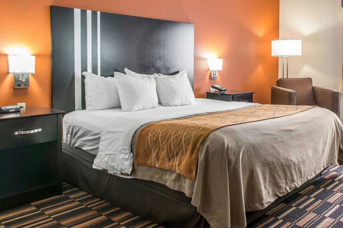 A hotel room with a large bed, two bedside tables, a chair, and a wall-mounted lamp.