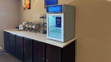 A self-service breakfast station with a refrigerator, a coffee machine, and a fruit dispenser.
