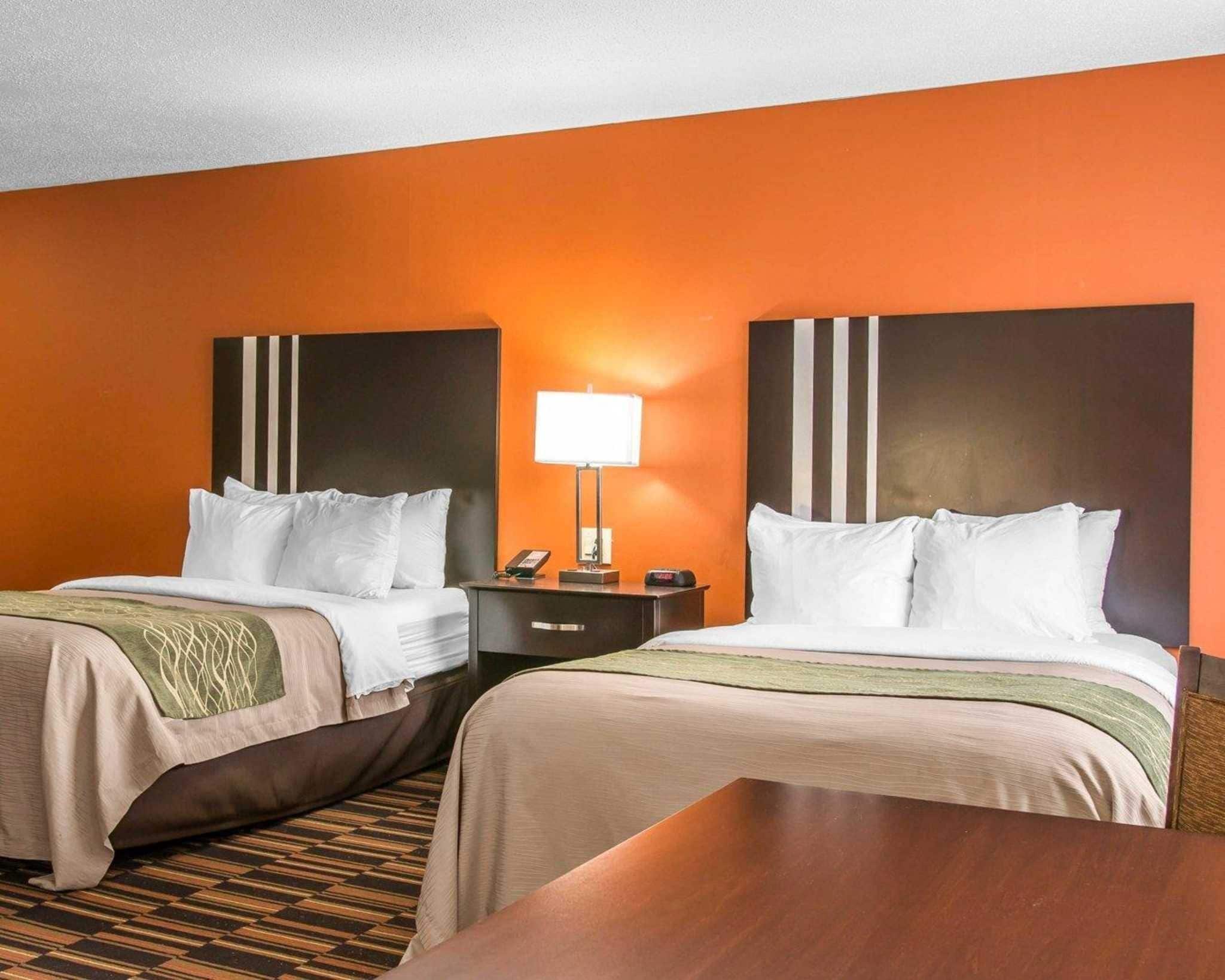 A hotel room with two beds, a nightstand with a lamp, and a wooden table.