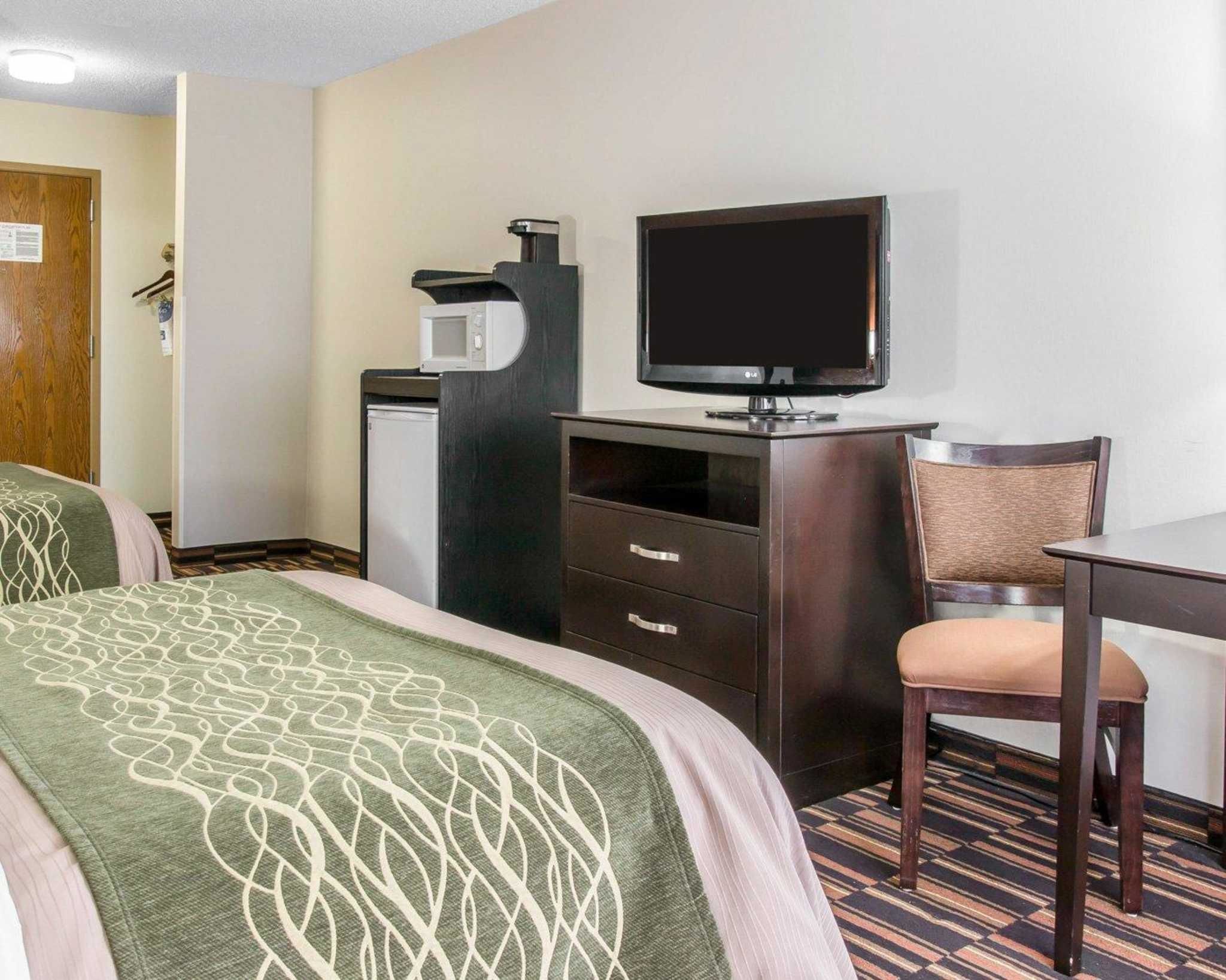 A hotel room with two beds, a desk, a chair, a television, and a coffee machine.
