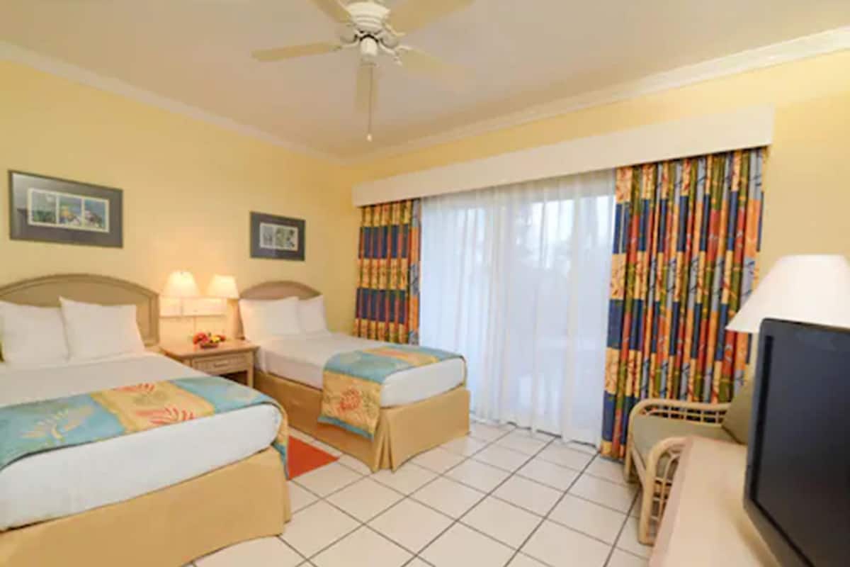 A hotel room with two beds, a ceiling fan, a TV, and a window with curtains.