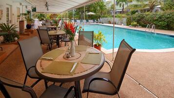 A poolside area with a round table, chairs, and a view of a swimming pool.