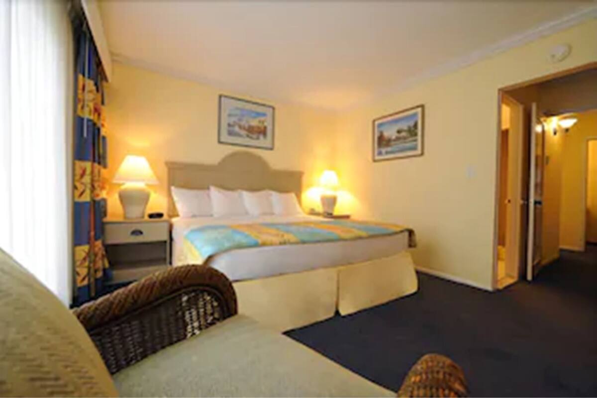 A hotel room with a bed, two bedside lamps, a nightstand, a chair, and a door leading to another room.
