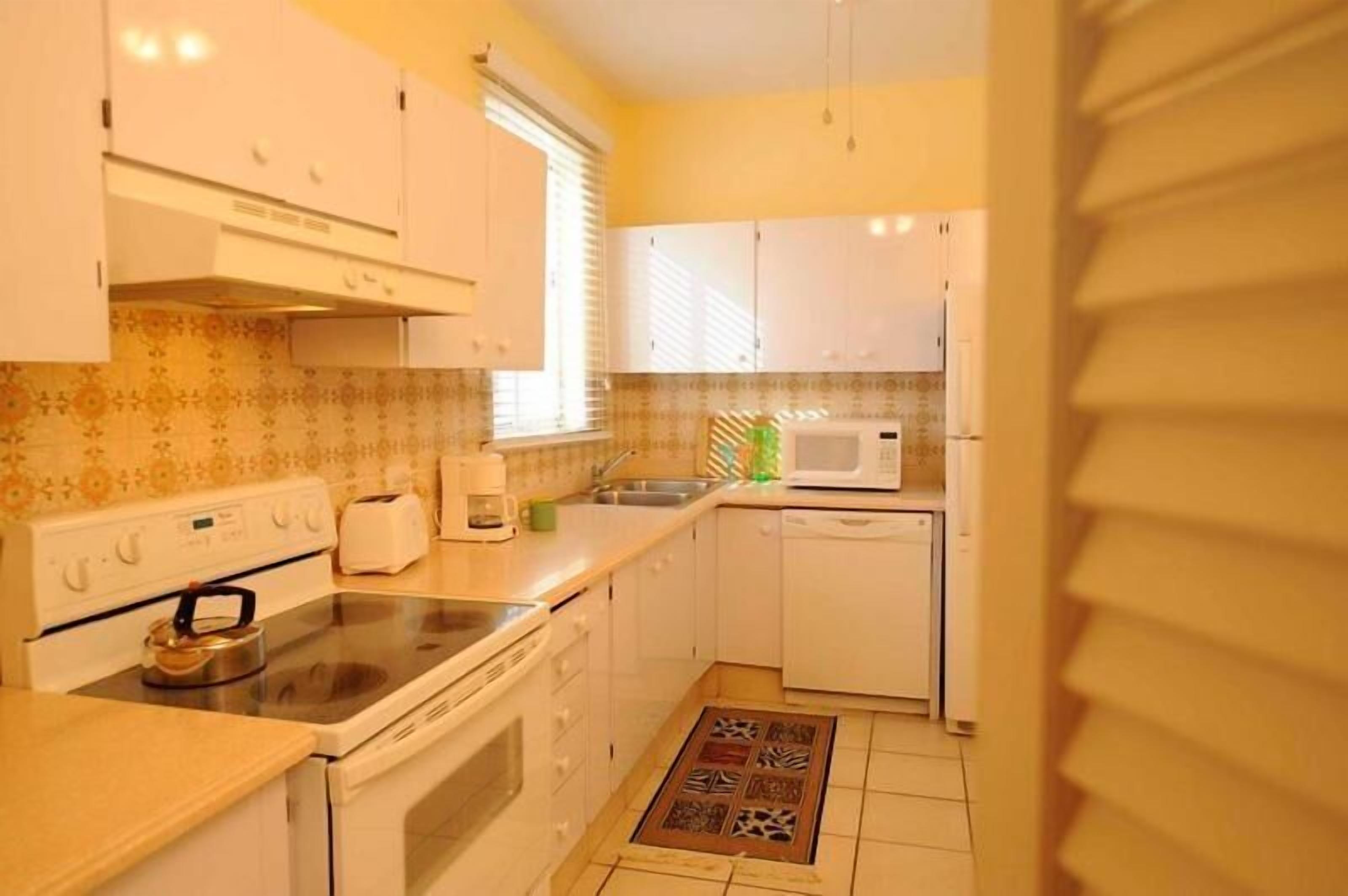 Une cuisine de taille réduite, avec des meubles blancs, une cuisinière, un four à micro-ondes et un évier.