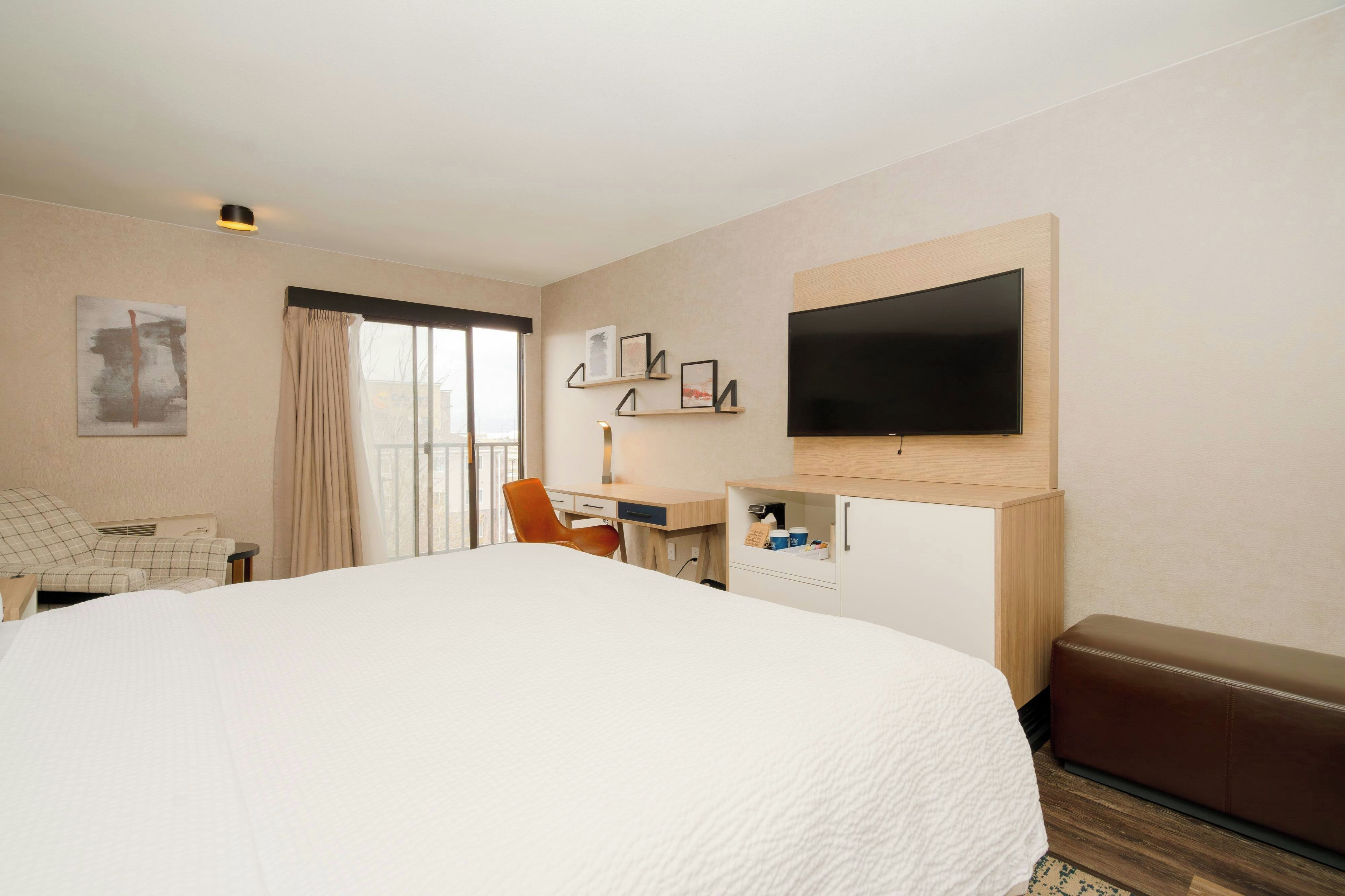 A hotel room with a large bed, a desk with a computer, a television, and a seating area with a brown leather couch.