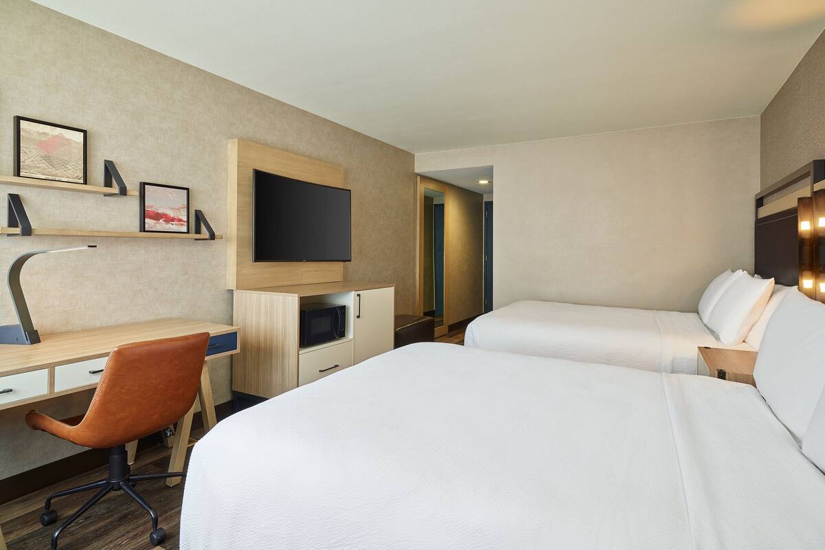 Ein Hotelzimmer mit zwei Betten, einem Schreibtisch mit Stuhl, einem Fernseher und einer Mikrowelle.