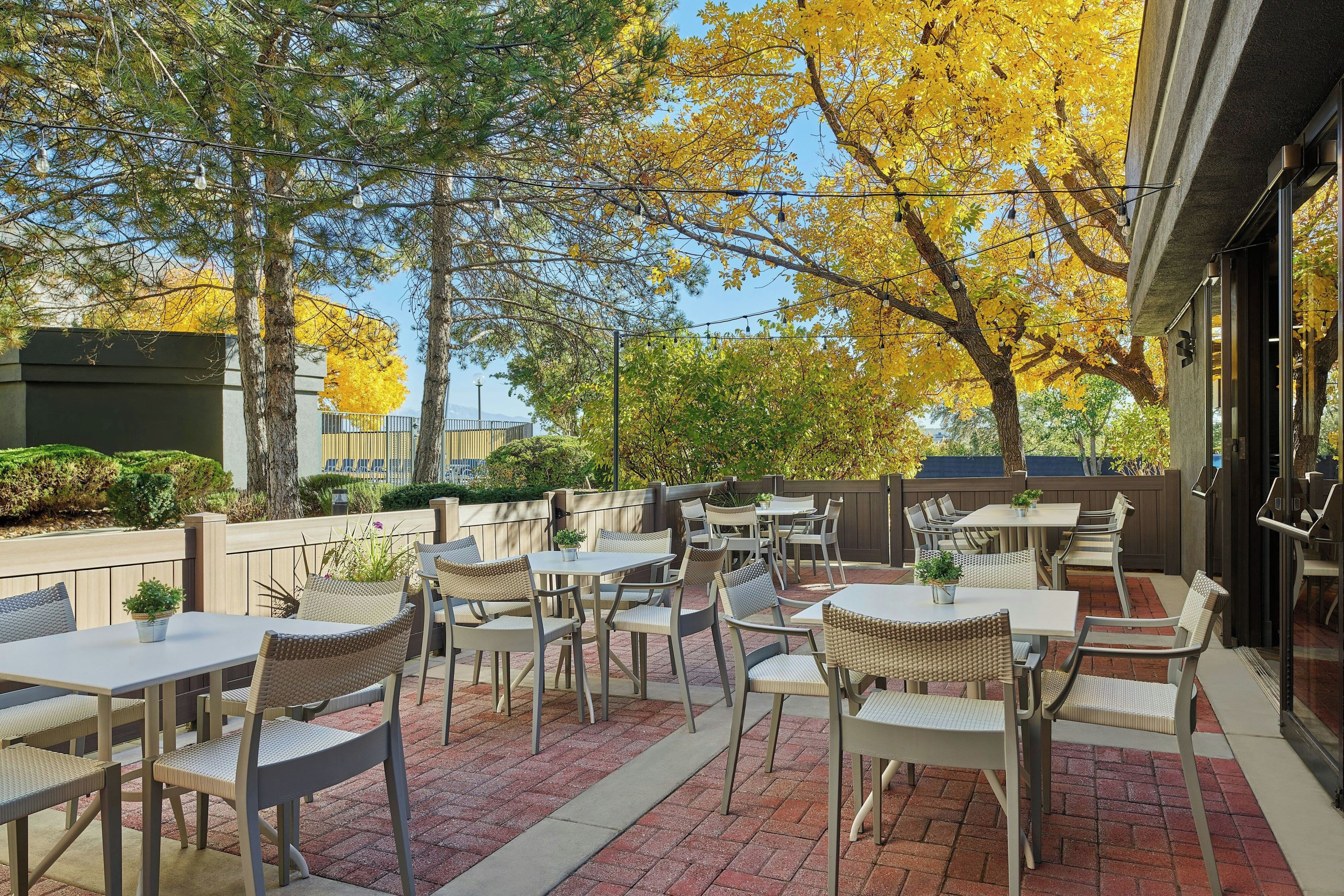 An outdoor patio with tables and chairs, surrounded by trees with yellow leaves.