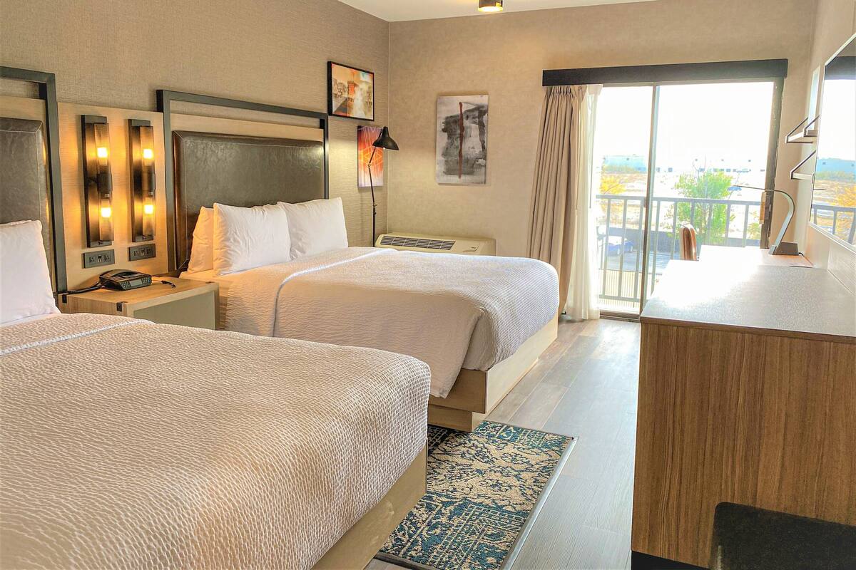Ein Hotelzimmer mit zwei Betten, einem Schreibtisch, einem Telefon und einem Fenster mit Blick ins Freie.