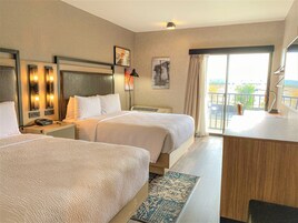 A hotel room with two beds, a desk, a telephone, and a window with a view of the outside.