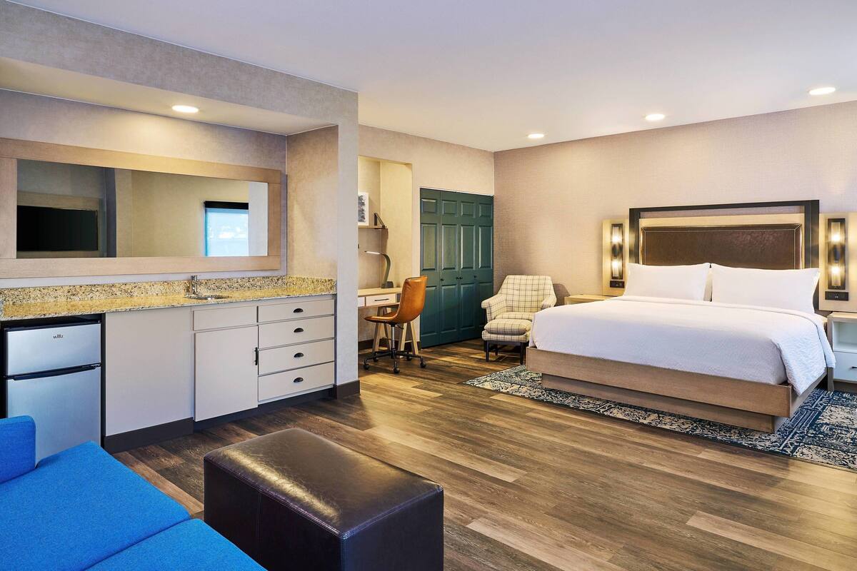 Ein Hotelzimmer mit Bett, Schreibtisch, Stuhl, einer kleinen Küche und einem Badezimmer.
