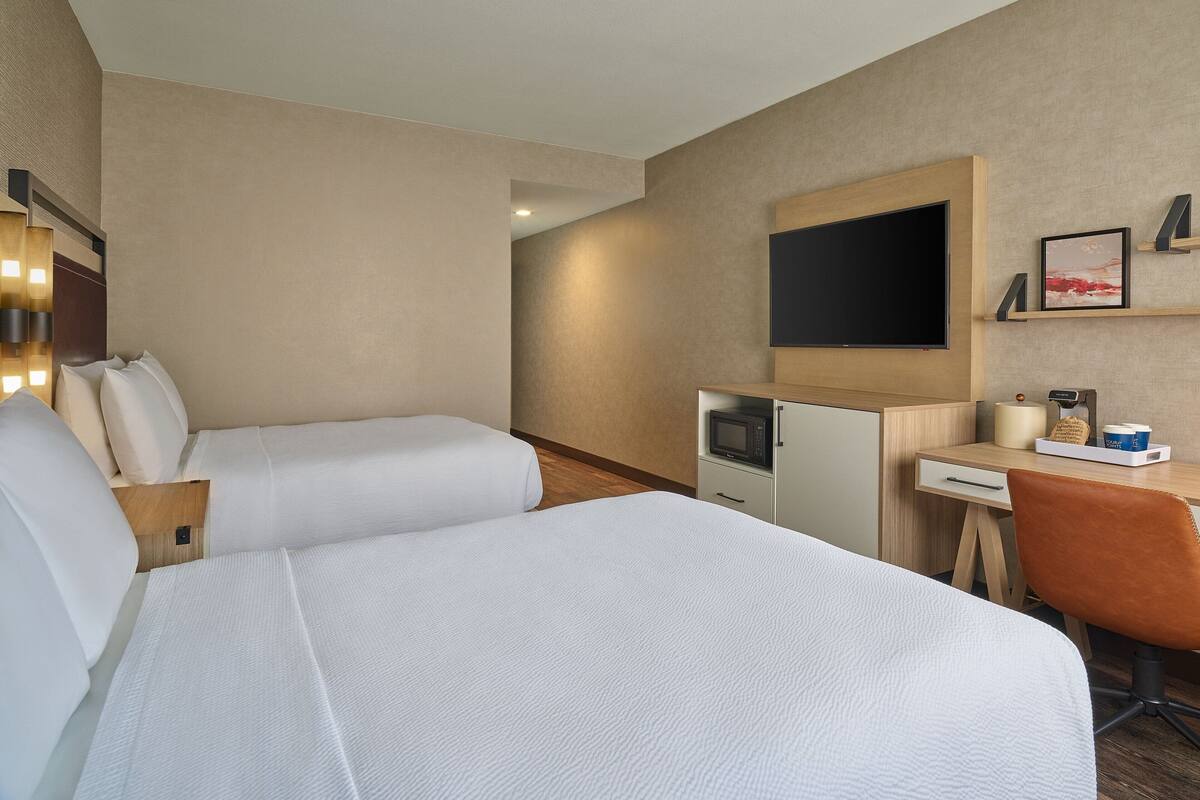 Ein Hotelzimmer mit zwei Betten, einem Schreibtisch, einem Fernseher und einer Mikrowelle.