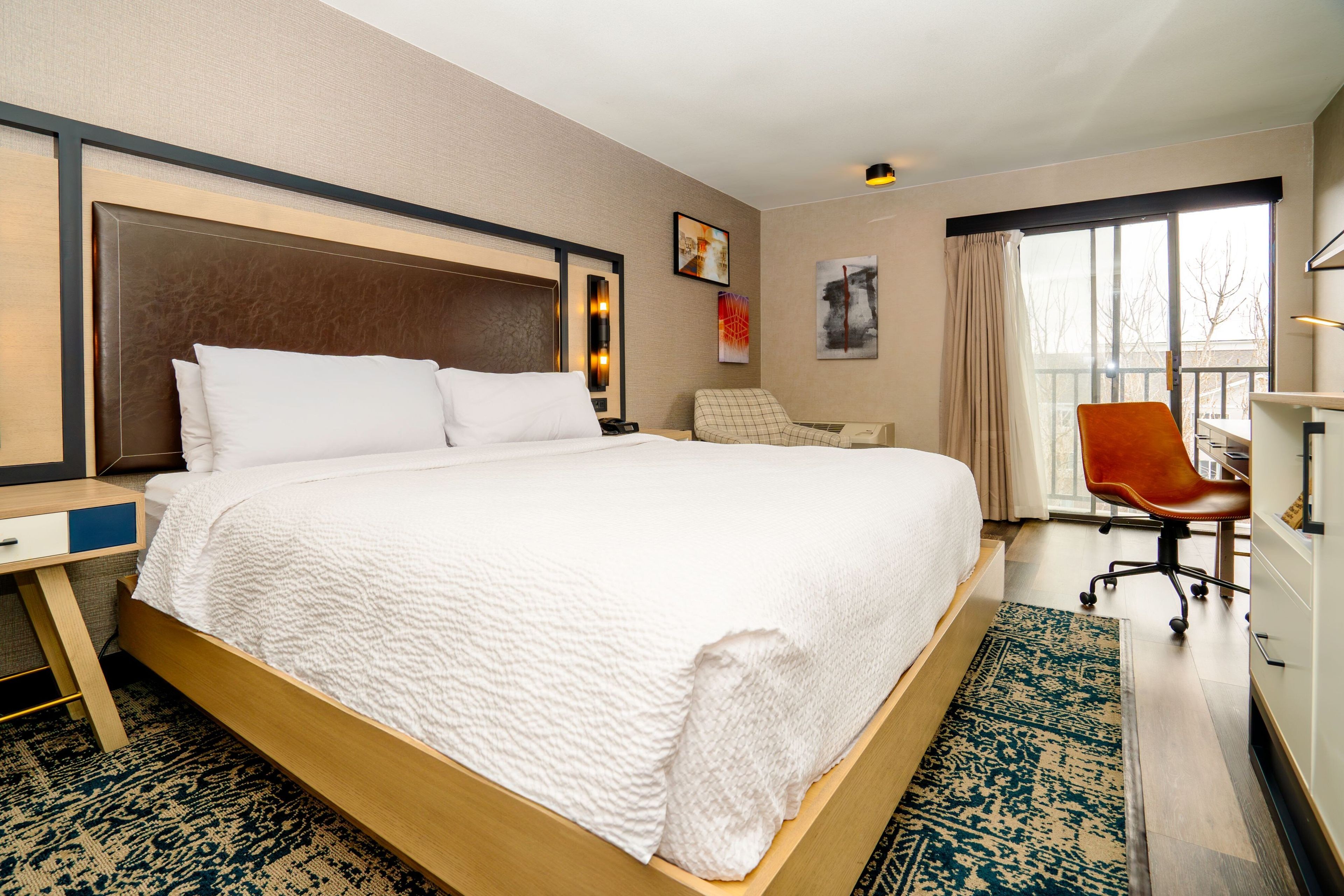 Une chambre d’hôtel avec un grand lit, un bureau, une chaise et une vue sur l’extérieur par une fenêtre.