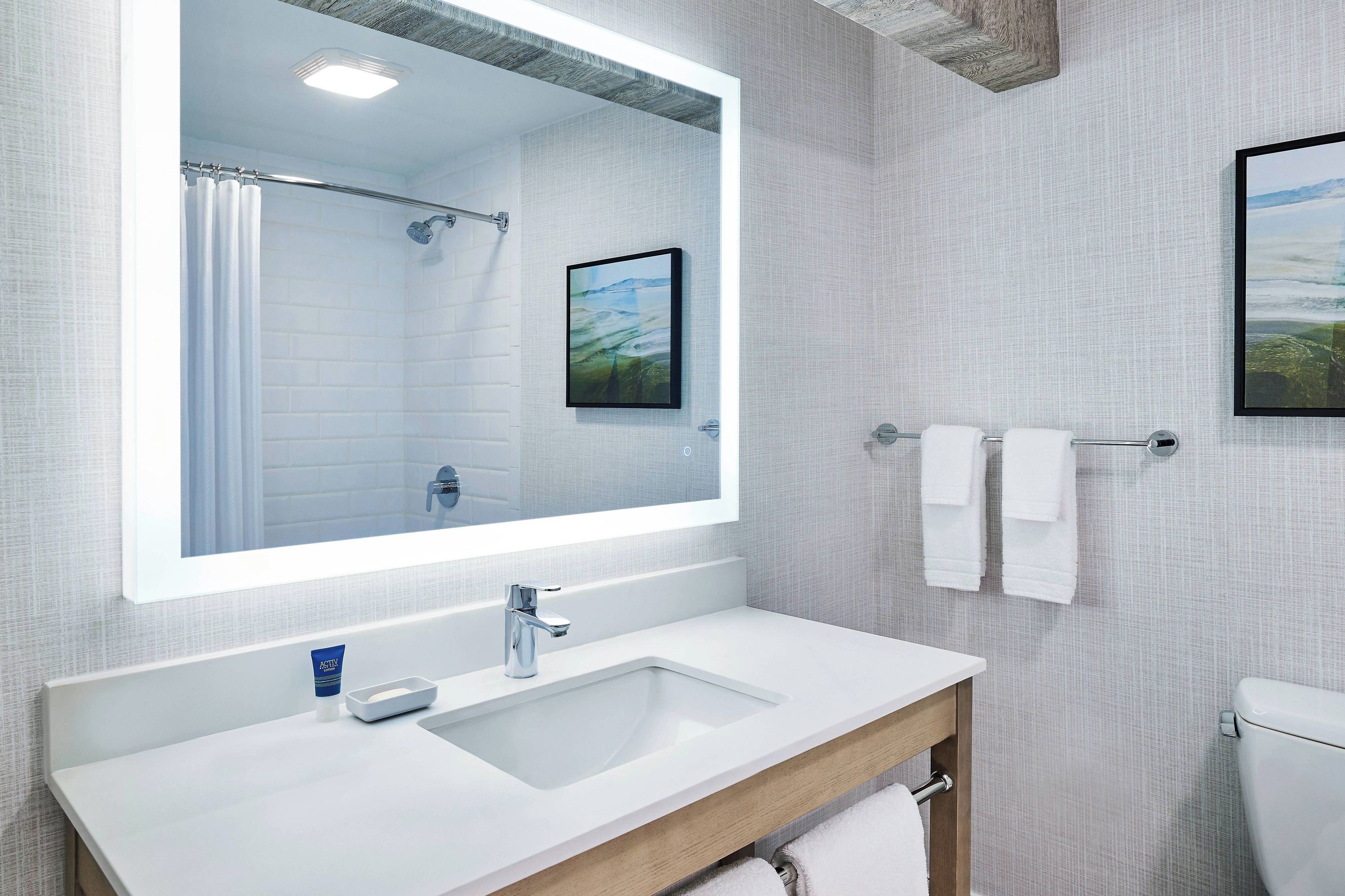 A modern bathroom with a large mirror, a sink, and a shower.