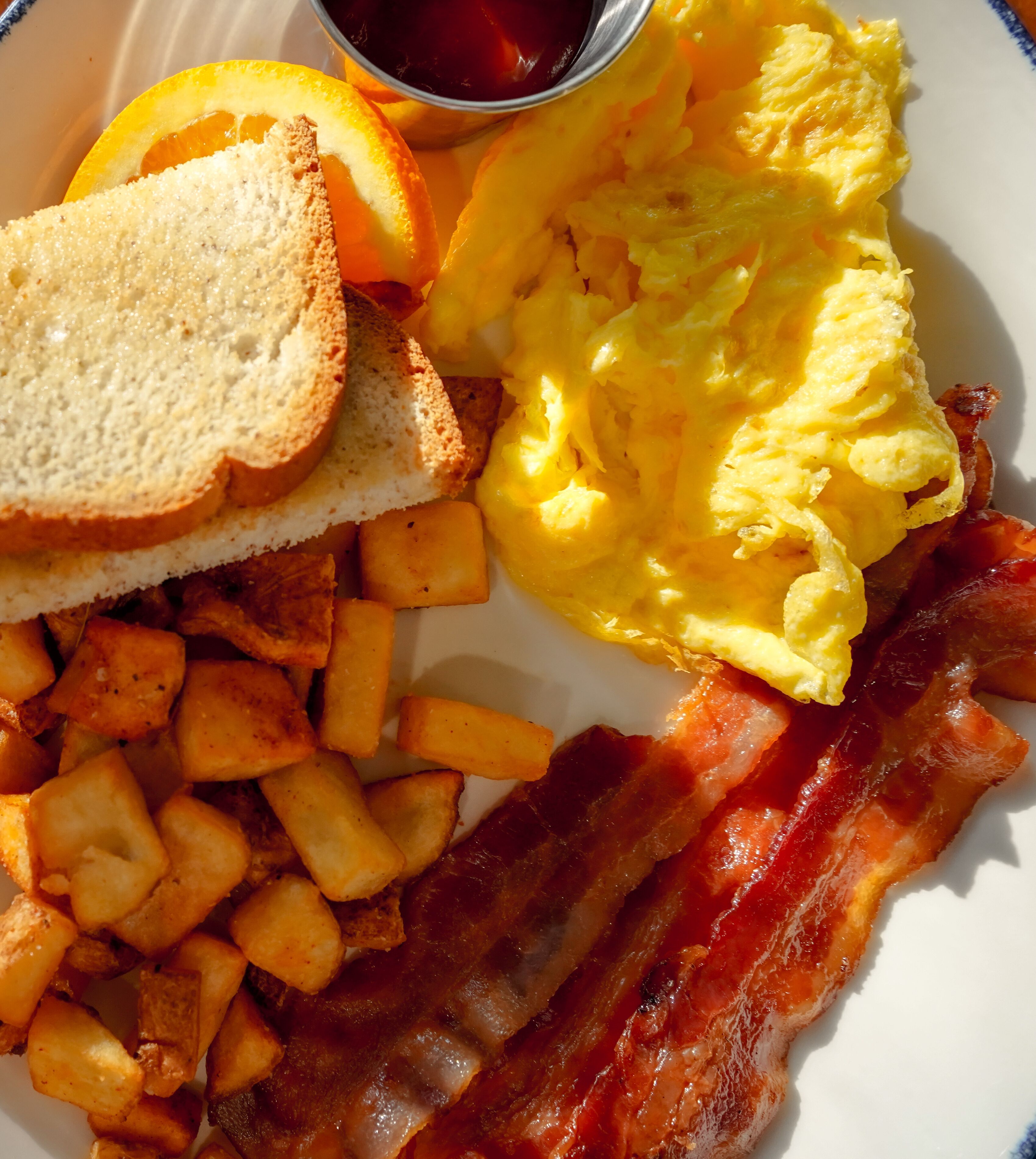 A breakfast plate with toast, scrambled eggs, bacon, hash browns, and orange slices.