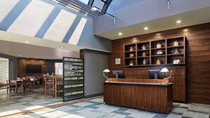 A modern hotel lobby with a reception desk, wooden shelving with decorative items, a dining area, and a large skylight. - Four Points by Sheraton Salt Lake City Airport (Salt Lake City)