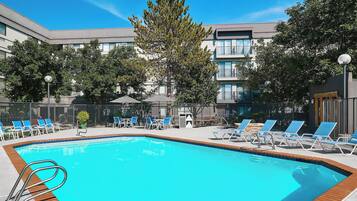 Una piscina con sillones de descanso y un edificio al fondo.