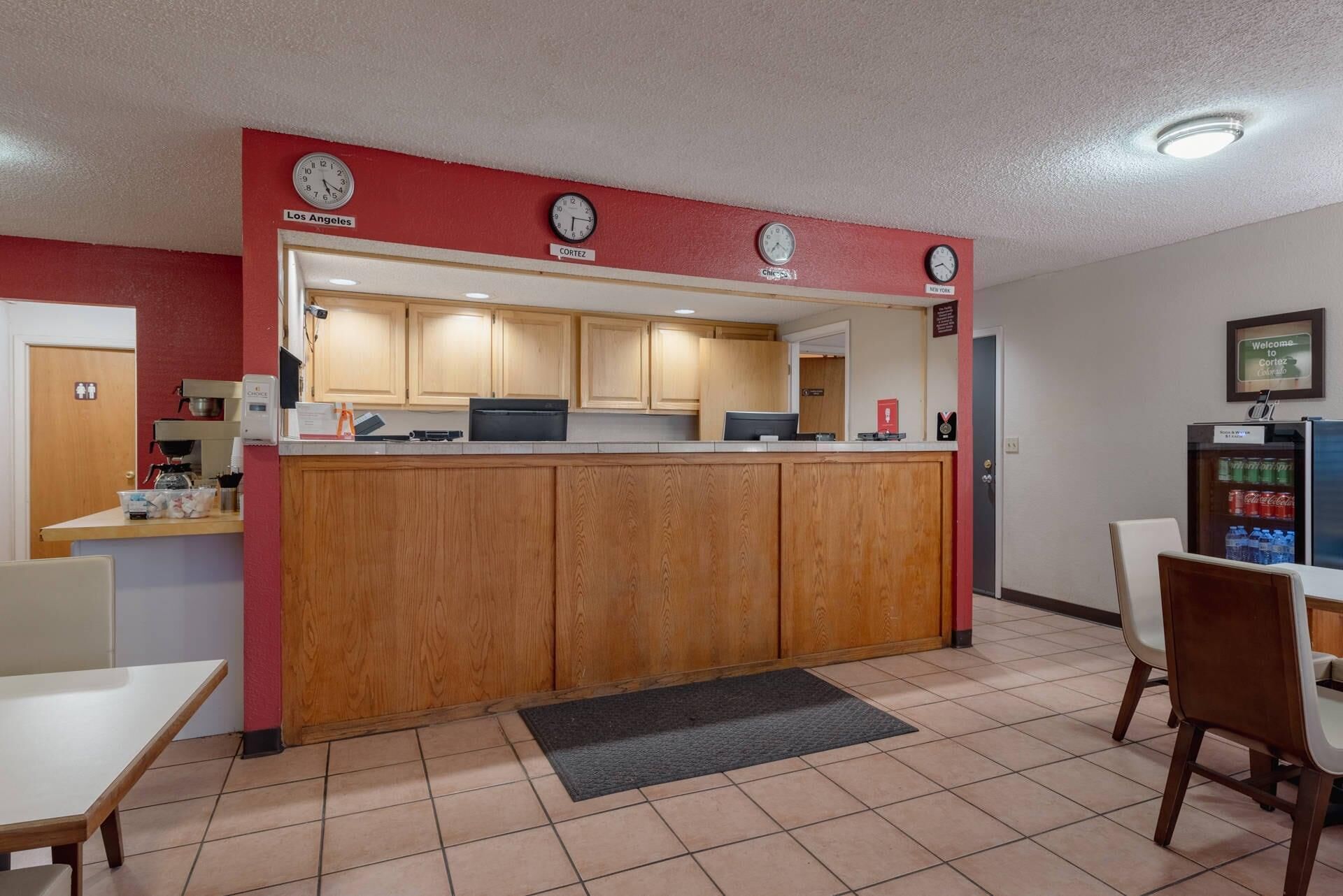 A kitchenette with wooden cabinets, a refrigerator, and a coffee machine. There are clocks on the wall displaying different time zones.
