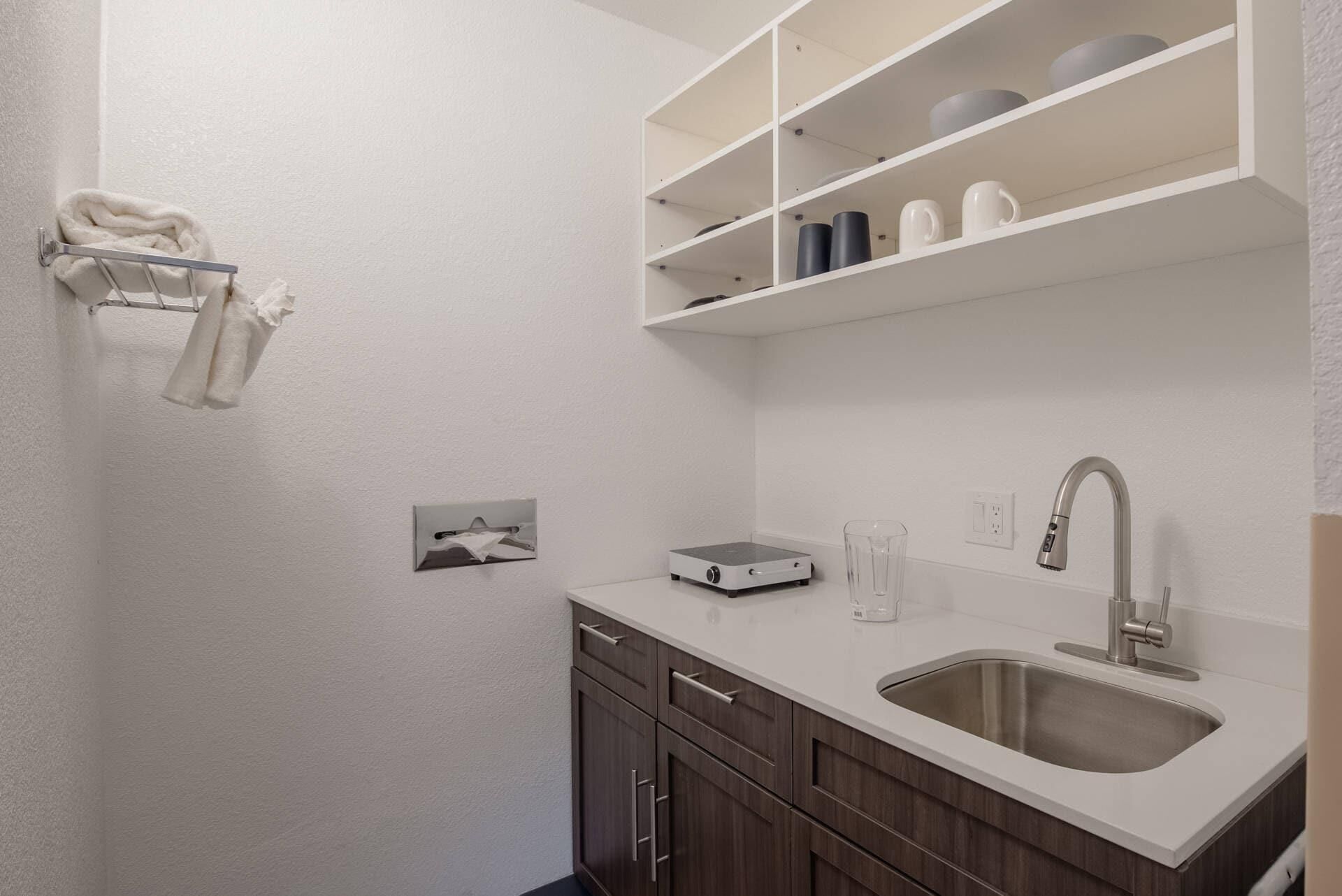 Una cocina moderna con encimera blanca, pileta de acero inoxidable y muebles de madera.