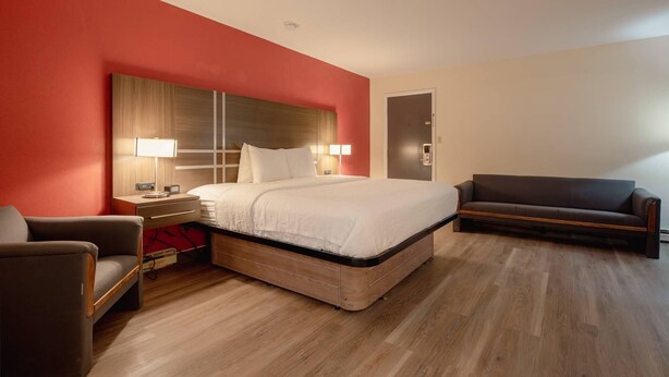 Une chambre d’hôtel avec un lit, une table de chevet, une lampe, un canapé et une porte.