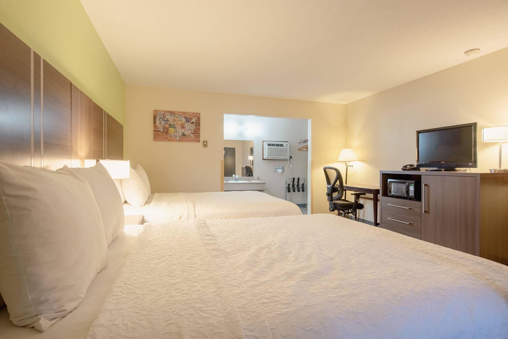 A hotel room with two beds, a desk with a computer, a TV, and a microwave.
