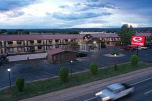 Un motel con un edificio central, una explanada de estacionamiento y una carretera con vehículos que circulan.