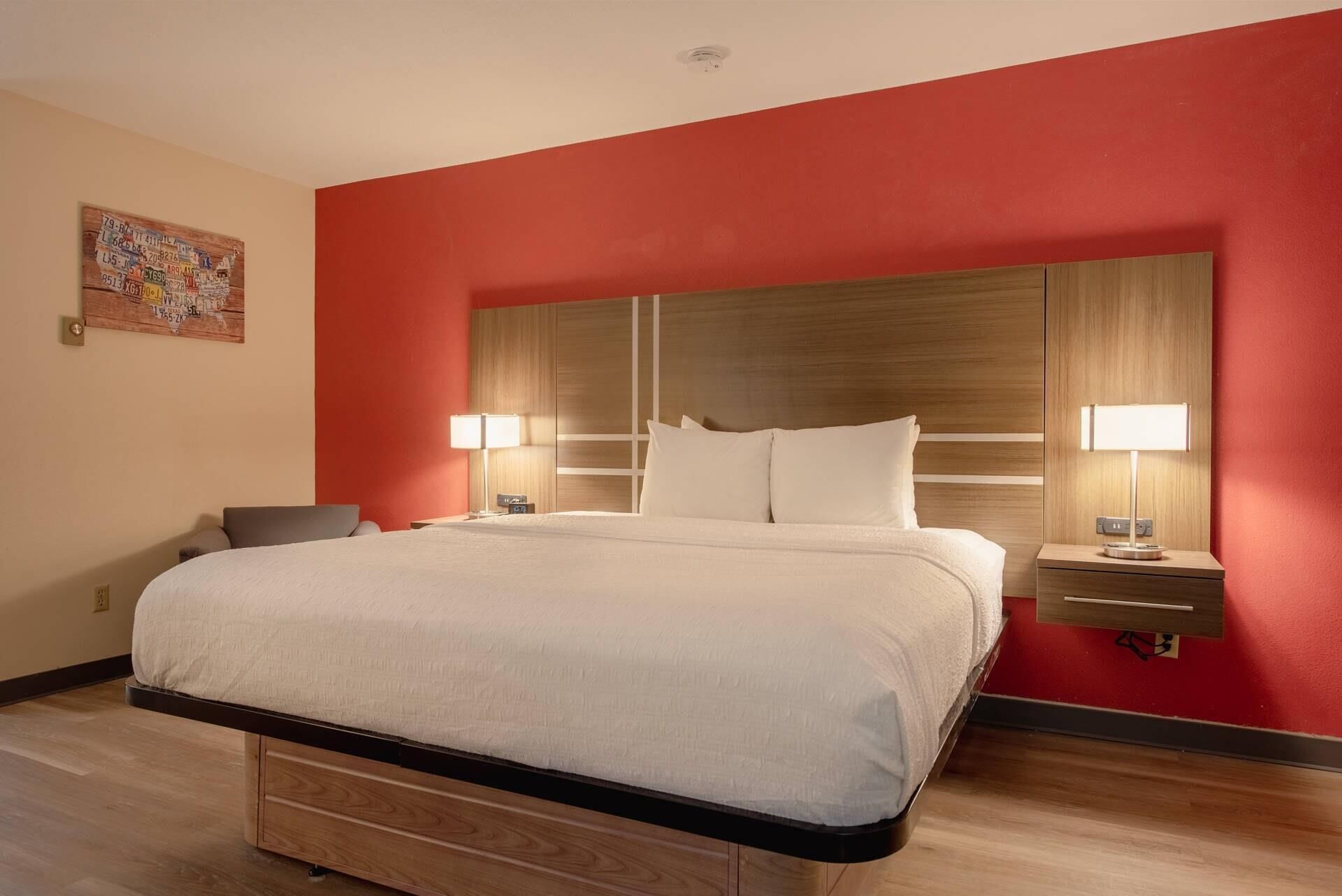 Quarto de hotel com uma cama grande, duas mesas de cabeceira com luminárias, uma cabeceira de madeira e uma parede vermelha.