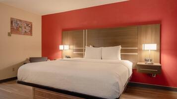 A hotel room with a large bed, two bedside tables with lamps, a wooden headboard, and a red accent wall.