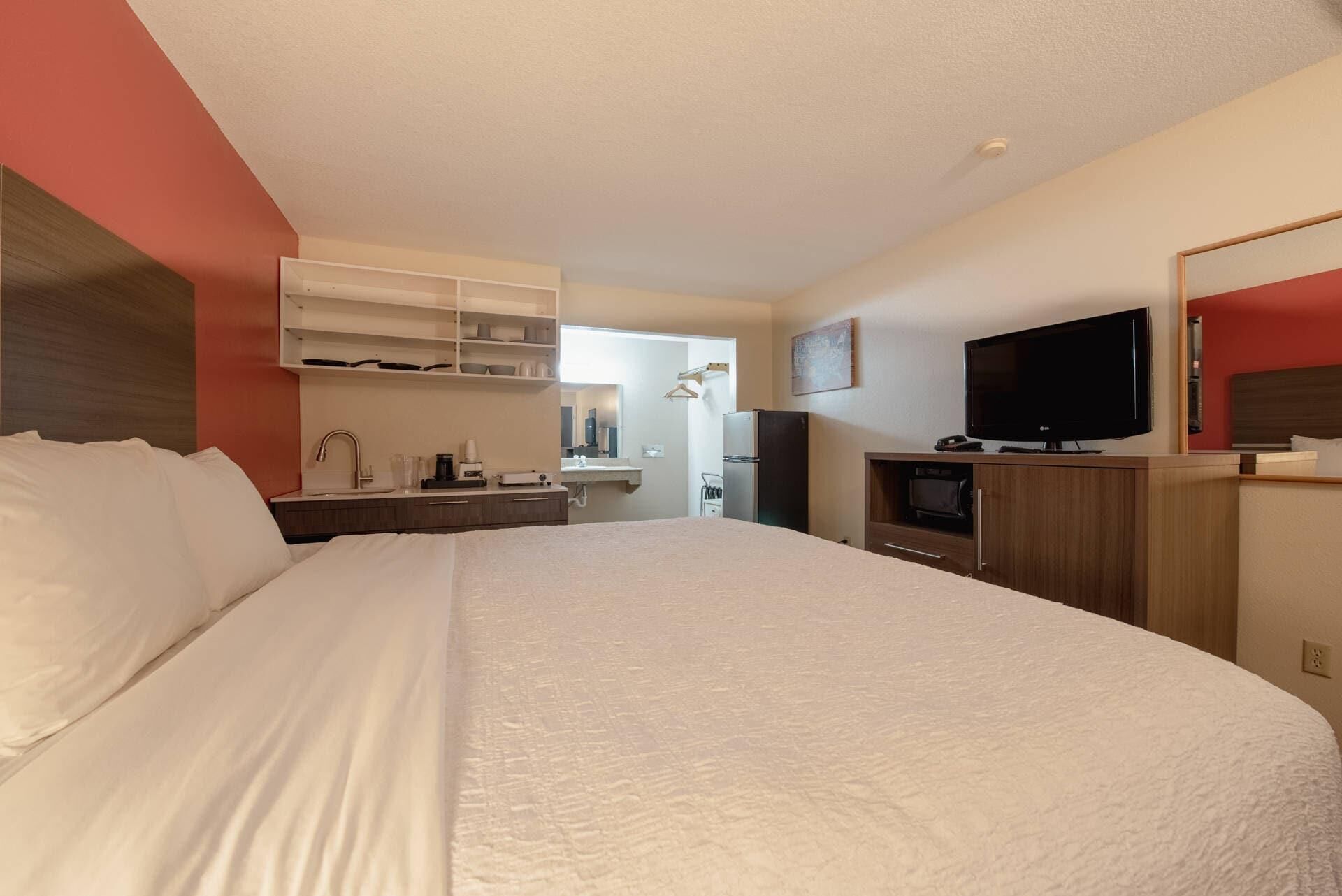 Habitación de hotel con una cama grande, televisión, refrigerador y kitchenette.