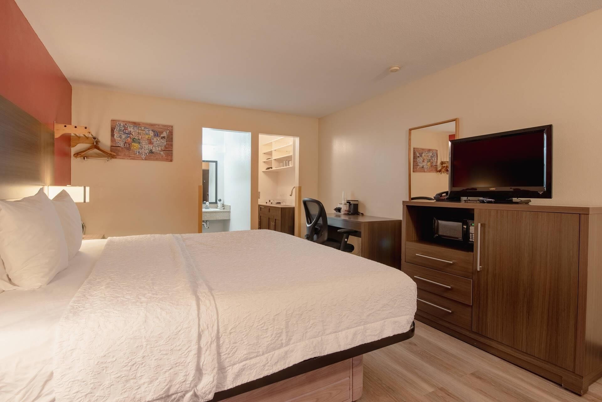 Ein Hotelzimmer mit einem Bett, einem Schreibtisch mit Stuhl, einem Fernseher und einer kleinen Küchenzeile.