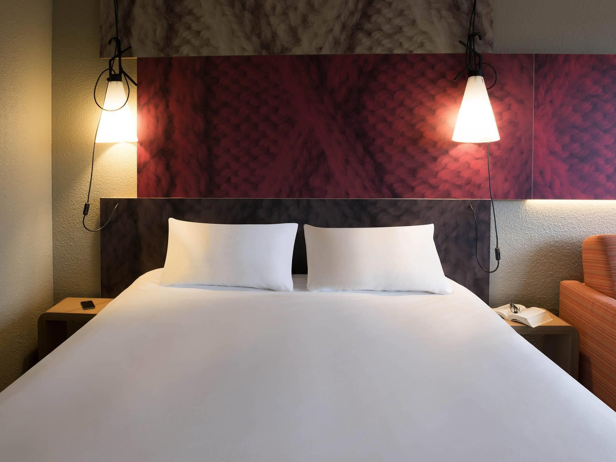 Un lit bien fait, avec deux oreillers, une tête de lit au motif texturé et deux lampes de chevet.