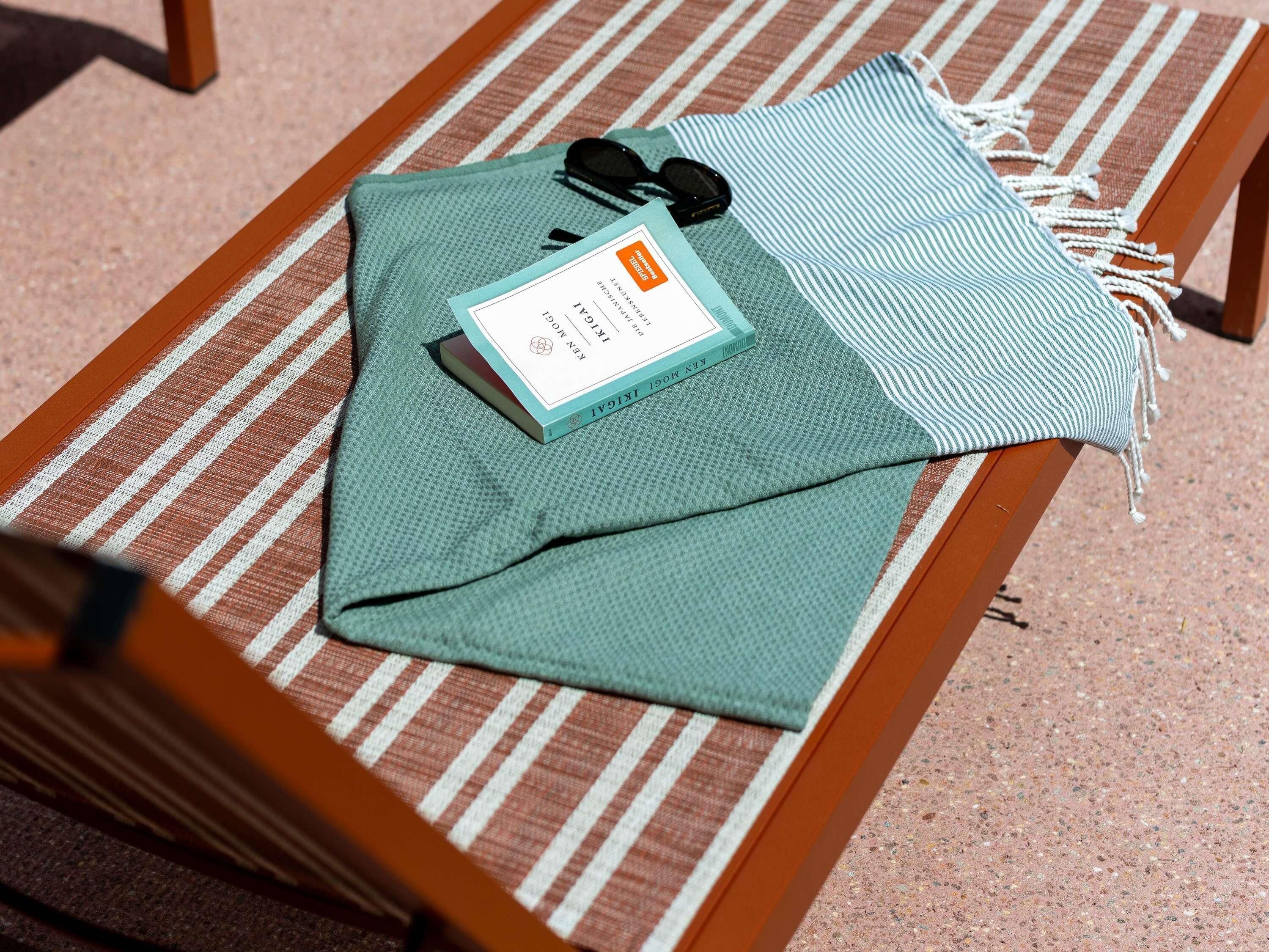 Tejido a rayas sobre una mesa de madera con un libro y gafas de sol.