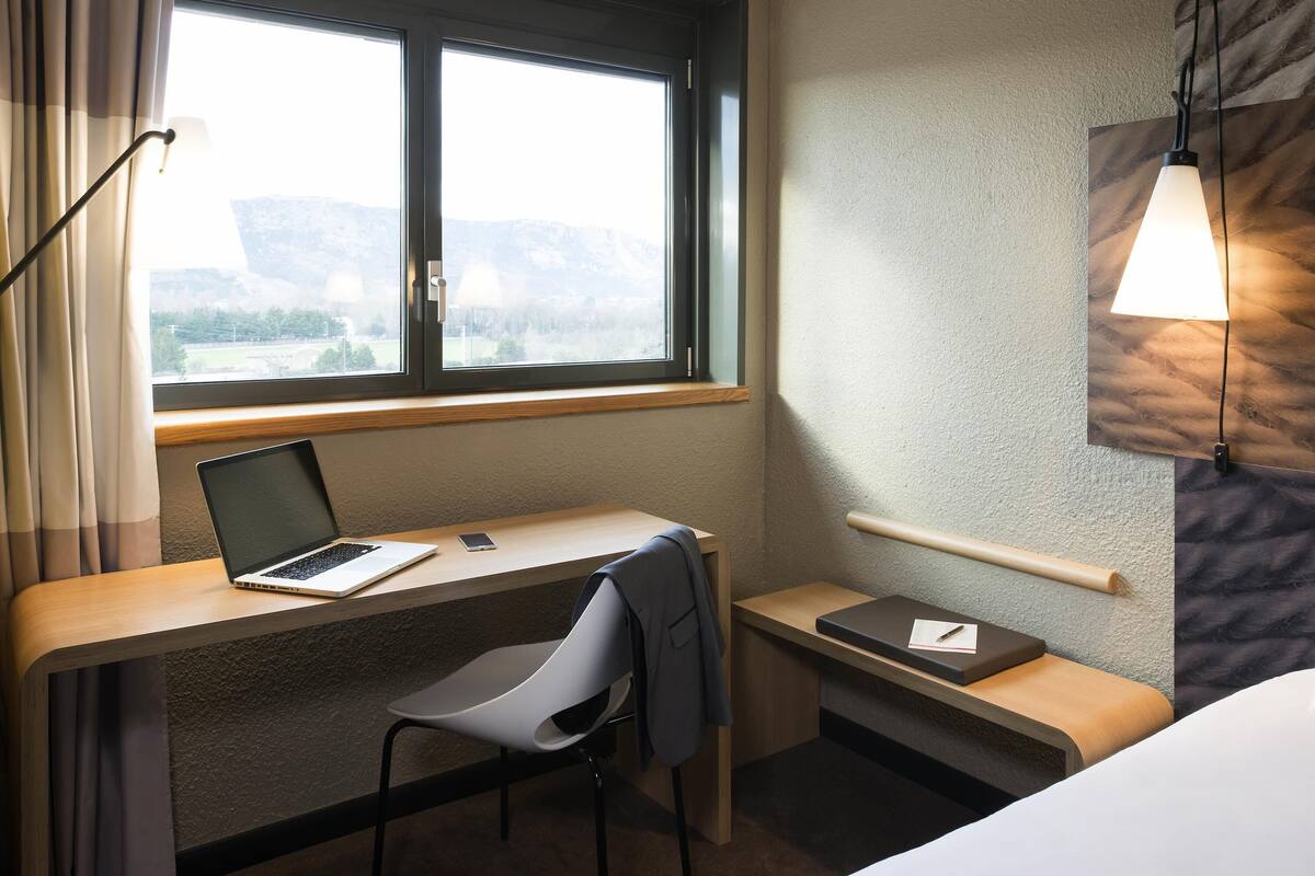 Une chambre d’hôtel équipée d’un bureau, d’une chaise, d’un ordinateur portable et offrant une vue sur les montagnes par la fenêtre.