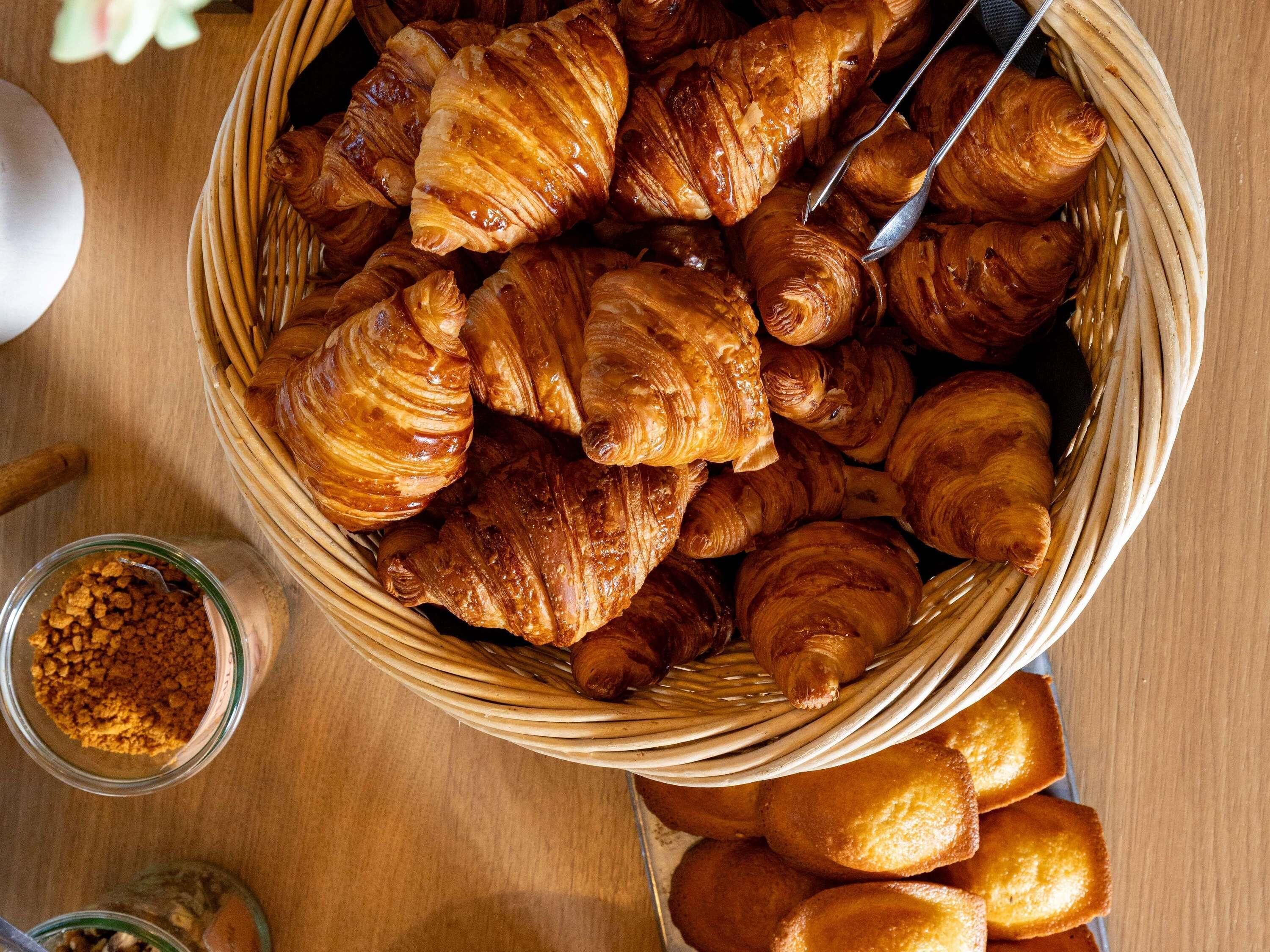 Ein Korb mit Croissants und eine Schüssel mit zerbröseltem Gebäck auf einer Holztisch.