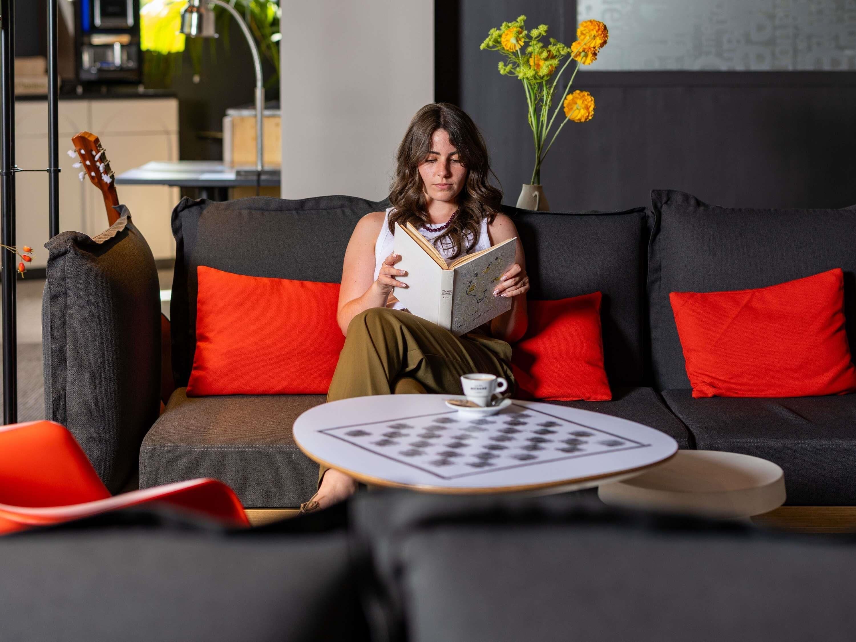 Une personne assise sur un canapé, avec un livre, une tasse et un jeu d’échecs.