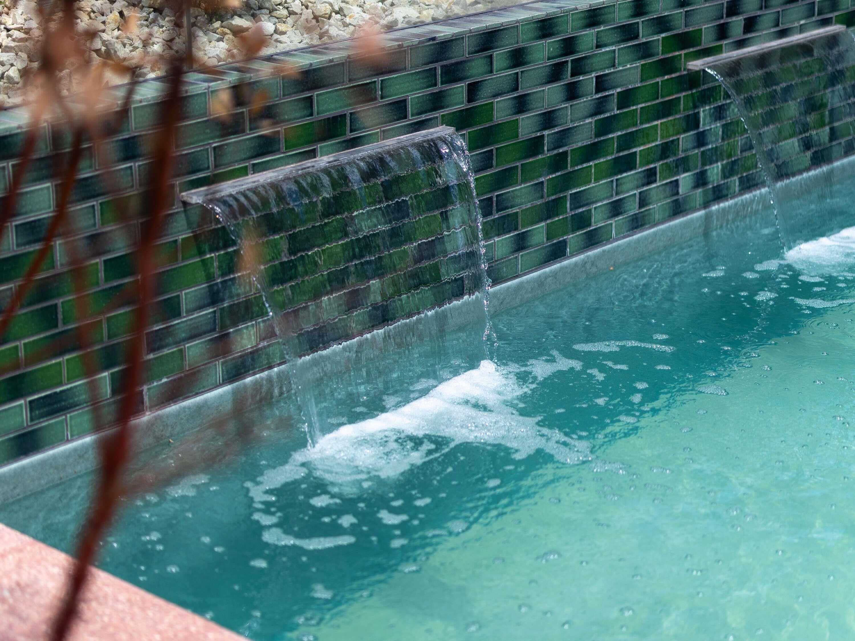 Una fuente de agua cristalina con pared de azulejos y piscina.