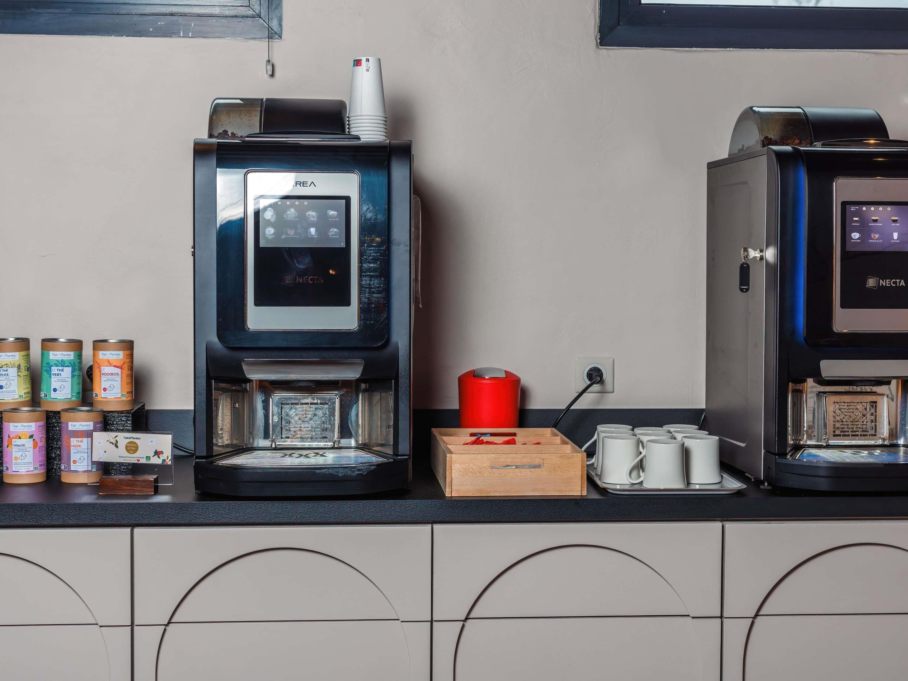 Deux machines à café, une poubelle rouge et un plateau avec des tasses blanches sur un comptoir.