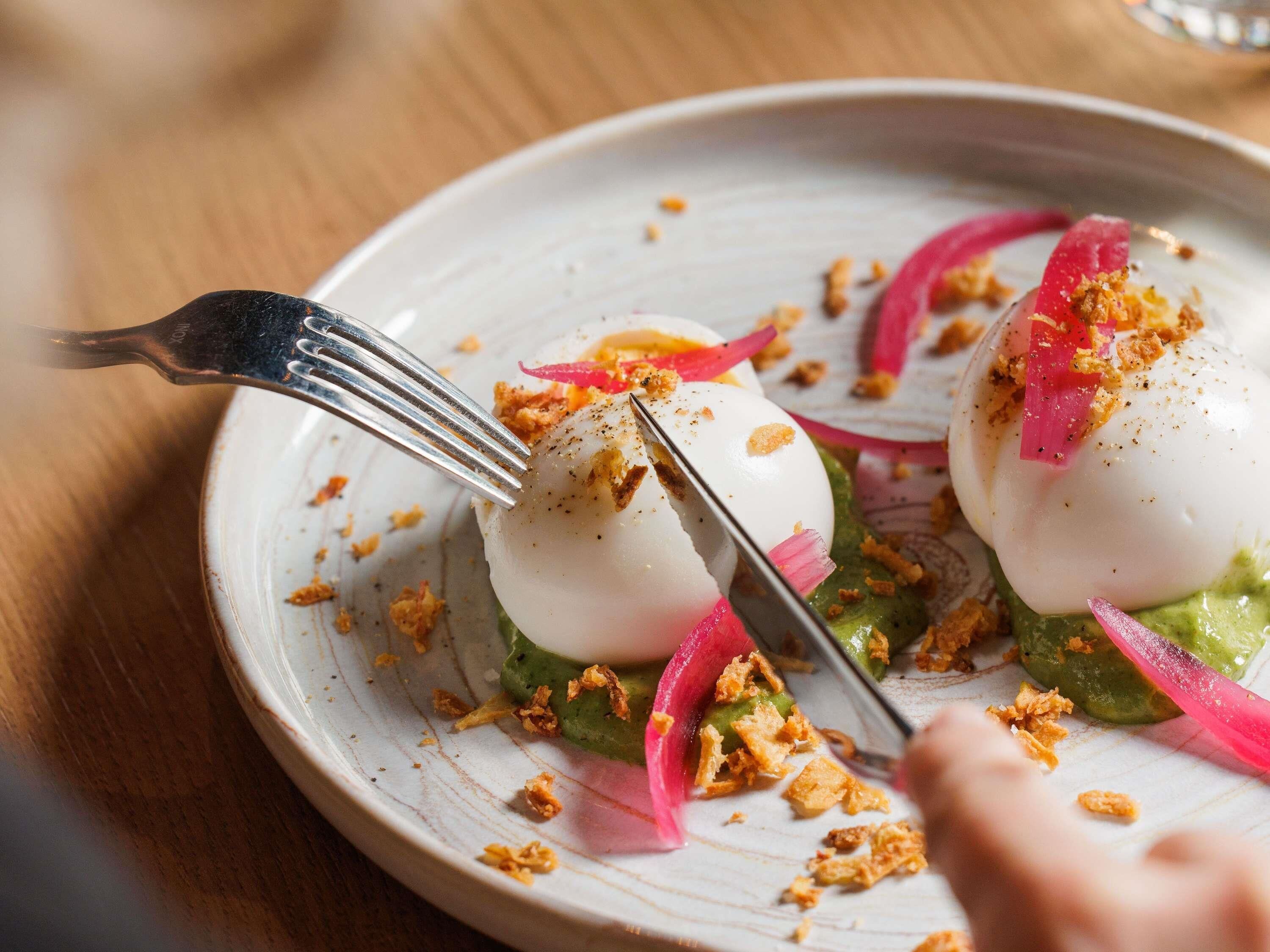 A plate with a poached egg, green sauce, and red onion garnish.