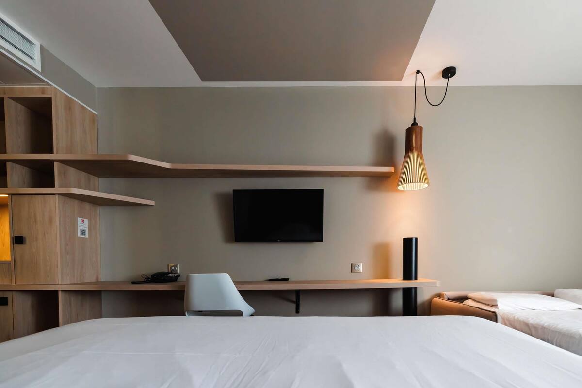 Une chambre d’hôtel avec un lit, un bureau, une chaise, une télévision et une lampe.