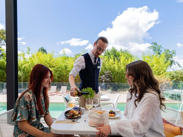 A dining table with food, a waiter pouring a drink, and a pool view.