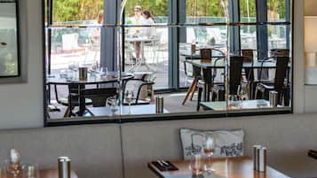 A restaurant with outdoor seating, large windows, and a view of greenery.